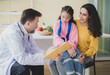 © Singh - Doctor man care caucasian sitting use stethoscope check girl sick illness daughter who came to hospital with mother woman three people with talk helping support give advice inside  treatment room