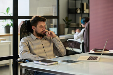 Poster - Young pensive businessman looking at laptop screen while analyzing online financial data in coworking space