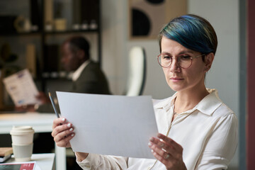 Aufkleber - young serious female economist in eyeglasses looking at paper document with financial charts while a