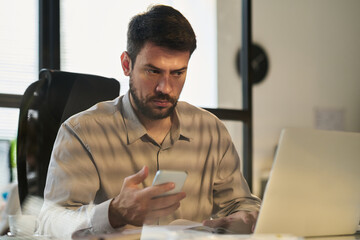 Poster - Serious male analyst looking at laptop screen and using mobile phone while watching online video or reading information