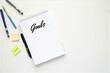 © draftseptember - A notebook with the word 'Goals' written on it, surrounded by pens, glasses, and sticky notes.