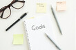 © draftseptember - A notebook with the word 'Goals' written on it, surrounded by pens, glasses, and sticky notes.