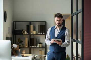 Aufkleber - Young serious businessman using tablet and looking at camera while standing in coworking space with desks and shelves