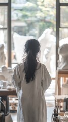 Poster - A person stands in a studio filled with sculptures, gazing out at a creative workspace.