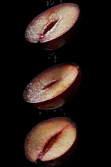 Poster - Three halves of a plum suspended in water droplets against a black background.