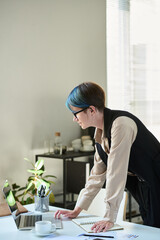 Aufkleber - Side view of young female ceo bending over workplace with laptop and looking at device screen while scrolling through data