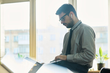 Aufkleber - Side view of young confident market analyst sitting in front of camera in office and looking through data on laptop screen