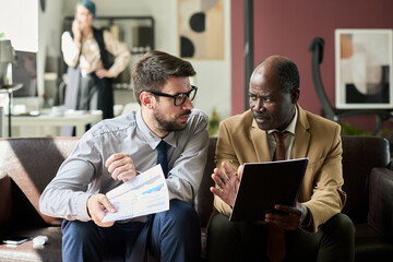 Aufkleber - Two young contemporary businessmen in formalwear sitting on couch in office and analyzing financial documents