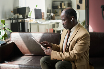 Poster - Mature African American male director of company sitting in front of camera in office and looking through document