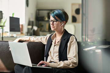 Aufkleber - Young serious female analyst with laptop on her knees sitting on leather couch in office and working with online data
