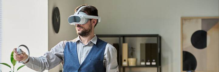 Poster - Header of young modern businessman with VR headset using controllers while making presentation of new project against colleague