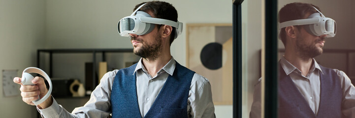 Poster - Panoramic of young male office worker in goggle using controllers during interactive presentation while standing in coworking space