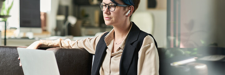 Aufkleber - Header of young serious female analyst with laptop on her knees sitting on leather couch in office and working with online data
