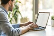 © Farizah - Young man working quietly at a modern desk with a laptop in a bright and airy office, focusing on tasks, surrounded by greenery and natural light.