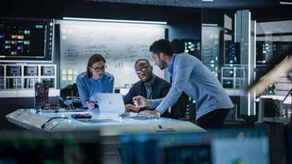 Diverse Team of Engineers Collaborating on Manufacturing Project in a Research Facility. Colleagues Analysing Data Using Laptop Computer and Brainstorming for a Technologically Advanced Invention