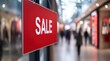 © Loolo - Close-up of a red sign with the text 'SALE' hanging in the blurred background of a modern shopping mall