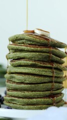 Wall Mural - Pouring maple syrup on top of homemade green pancakes with spinach and banana. Vertical video. Close-up. Heatlhy breakfast of dessert food.