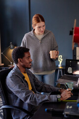 Fototapete - Multiracial colleagues collaborating on project in cozy office space with modern equipment, engaging in focused discussion while reviewing digital content on laptop screen