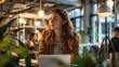 © Prostock-studio - In a contemporary office filled with natural light, a woman with long hair sits at a table, concentrating on her work. She is surrounded by plants and other professionals engaged in their tasks.