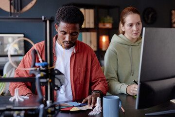 Leinwandbilder - Man and woman working on 3D printing project, focusing on creating model with precision while discussing details. Office setting features modern tools and relaxed atmosphere