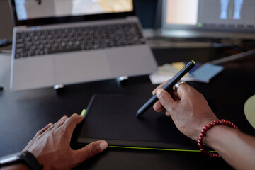 Fototapete - Person holding stylus working on graphics tablet. Digital artist creating design on tablet with laptop and other devices visible in background