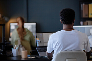 Fototapete - Two people working in a modern office with computers and various electronic devices. One person is seated at desk while another is blurred in background