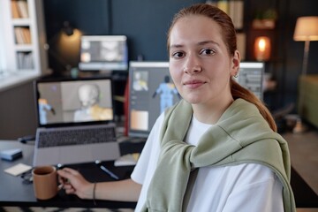 Leinwandbilder - Portrait of young woman sitting at her desk, holding coffee mug, with computer monitors in background, showing her engaged in creative work environment