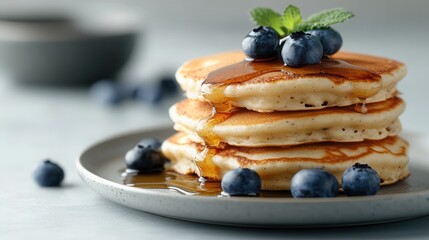 Wall Mural - Fluffy pancakes stacked high with fresh blueberries and drizzled with golden maple syrup on a light gray background