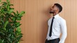 © ANGEL4289 - A stylish man in formal attire stands against a wooden wall, gazing upwards, next to a lush green plant.