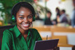 © carolina - An African woman call center agent, wearing a green blouse, smiling brightly while using a headset and laptop for customer service. Ideal for stock use in tech, communication, and professional setting