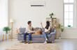 © Studio Romantic - Young couple, happy family with dog on sofa switching on air conditioner, blowing warm, cold air room temperature control for optimal home environment, providing ideal climate control heating system