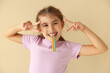 © New Africa - Happy girl eating tasty rainbow sour belt and showing peace signs on beige background