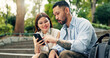 © peopleimages.com - Couple, phone and happy on travel at park on stairs, click and decision for hotel booking with mobile app. People, man and woman with smartphone, reading and notification on social network in Japan
