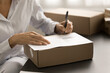 © fizkes - Post office manager woman preparing delivery document, writing notes on paper cardboard box for transportation, sending parcel, package, purchase to Internet store customer