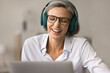 © fizkes - Positive happy pretty mature woman in glasses and big wireless headphones sitting at laptop, talking on video conference call, laughing at display, discussing business project, education