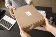 © fizkes - Delivery office employee giving parcel to customer at storage office workplace, holding package over work table. Internet store client getting purchase in store, taking cardboard box