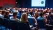 © Vader Stocker - Audience of people seated in a conference room, focused on a woman in the center.
