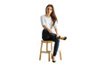 © peshkova - Woman wearing casual white sweater and jeans sitting on a wooden stool, isolated on a white background. Concept of casual style and confidence