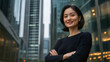 © Tetyana - Successful asian businesswoman smiling with folded arms in front of skyscrapers