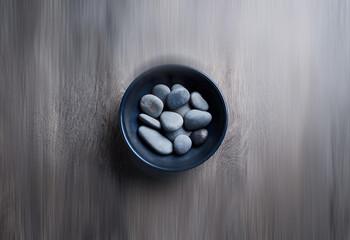 Poster - A dark bowl sits on a wood surface, holding a collection of smooth, grey stones.  The scene is minimalist and serene.