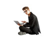 © peshkova - Young man in glasses wearing a formal outfit seated on the floor while using a laptop, isolated on a white background, concept of work