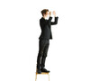© peshkova - Full-length image of a man in asuit standing on a wooden chair, reaching upward, against a white background. Concept of effort or problem-solving