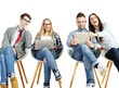 © peshkova - Four young adults sitting on chairs, interacting with laptops and tablets, casual clothing, white background. Concept of teamwork and technology