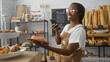 © Krakenimages.com - Woman happily taking photo with mobile phone in bakery shop holding a plate with pastries surrounded by bread and baked goods