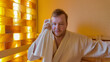 © fotoworld - A Caucasian man relaxes in a sauna, using a towel to unwind and improve wellness during a spa retreat