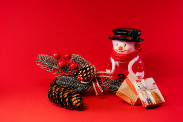 Wall Mural - Festive arrangement with a snowman figurine, pinecones, and gifts on a red background.