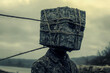 © DrCreative - A human figure with a stone block as a head, tied with ropes, in a moody outdoor setting