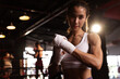 © kamonrat - Confident Female Boxer Wrapping Hands in Gym, Preparing for Training Session, Strong and Determined, Focused Athlete in Boxing Environment, Dedication and Fitness Lifestyle, Boxing Workout Prep