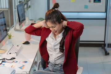 Wall Mural - Stressed asian businesswoman massages neck at office desk, highlighting discomfort from long hours at computer. Image shows need for healthcare in workplace