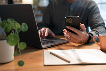 Wall Mural - Man working from home, using mobile phone and laptop computer sits at home office.